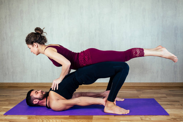 beautiful woman with curly hair and a muscular man practicing yoga together on the yoga mat . concept of tantric yoga and love. couple in love practicing asan yoga - Foto, Imagen