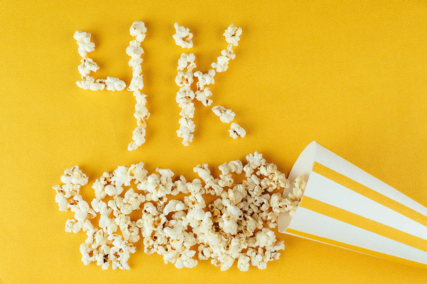 popcorn scattered on yellow background inscription 4k . The concept of home movies and movies in the cinema. quality of cinema. popcorn from corn kernels - Photo, image