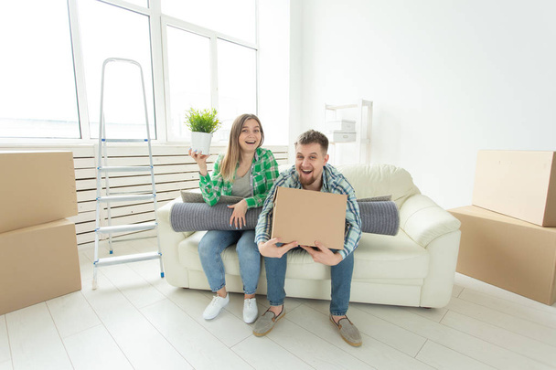 Cheerful joyful young couple charming girl and handsome man holding a box with things and a pot with a plant while moving to a new apartment. Housewarming and mortgage concept. - Photo, Image