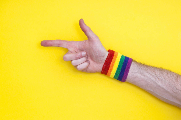 Pointing hand with gay pride rainbow flag wristband on a yellow  - Zdjęcie, obraz