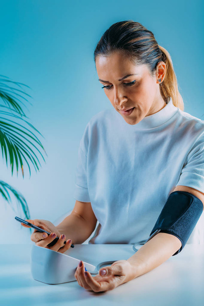Mobiele gezondheid - vrouw meten van de bloeddruk en invoeren van gegevens in de Smart Phone - Foto, afbeelding
