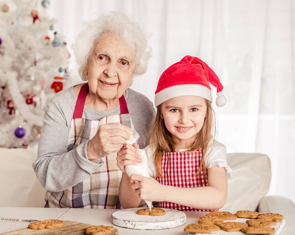 Grandmother with granddaughter holding baked cookie - Фото, изображение