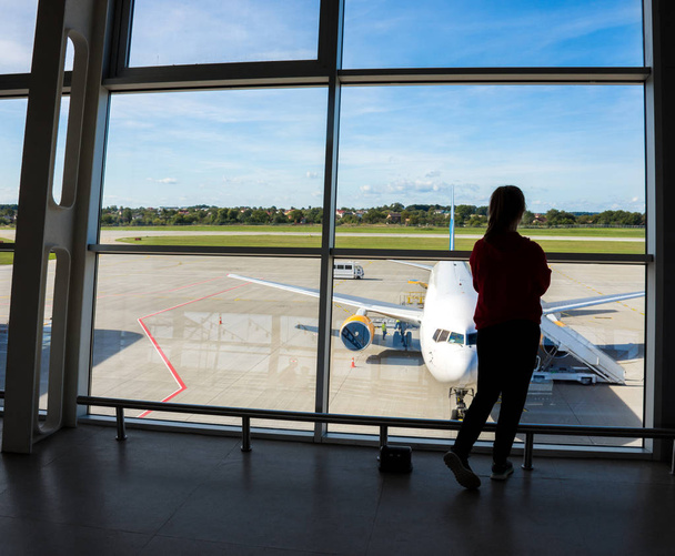 Νεαρή γυναίκα ταξιδιώτης κοιτάζοντας μέσα από το παράθυρο του αεροδρομίου στο Πλα - Φωτογραφία, εικόνα