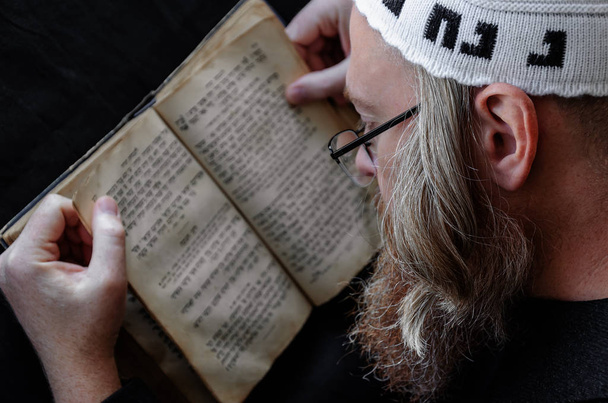 Een Hasidische Jood leest Siddur. Religieuze orthodoxe jood met een rode baard en met tempo in een witte baal bidden. Op de baal is een inscriptie Rabbi Nahman van Oeman. Close-up - Foto, afbeelding