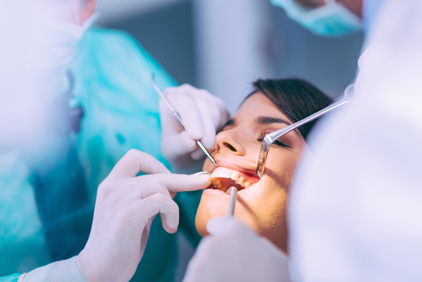  Οδοντίατροι που εργάζονται με νεαρή γυναίκα ασθενή - Φωτογραφία, εικόνα