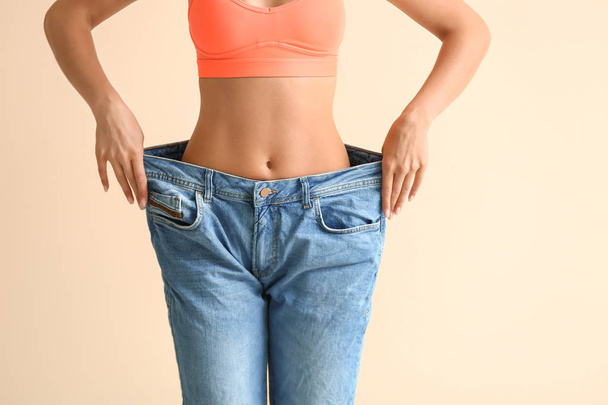 Beautiful young woman in loose jeans on color background. Weight loss concept - Foto, Bild