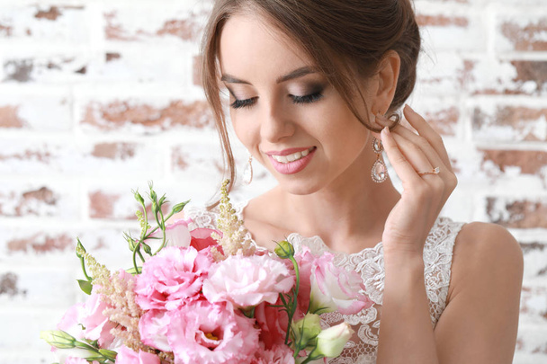 Portrait of beautiful young bride with wedding bouquet on brick background - Photo, Image
