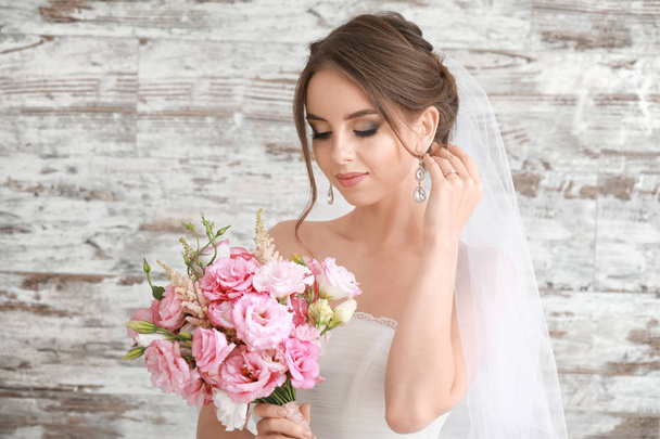 Portrait of beautiful young bride with wedding bouquet on wooden background - Fotó, kép