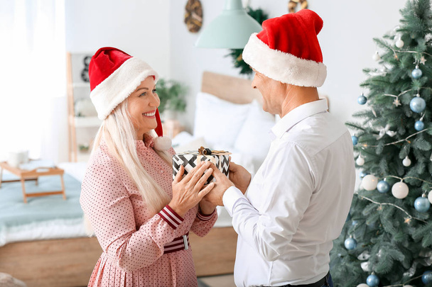 Зрелый муж дарит жене рождественский подарок дома
 - Фото, изображение