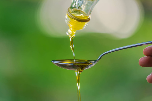 Versare l'olio d'oliva nel cucchiaio sullo sfondo del giardino del parco verde
 - Foto, immagini