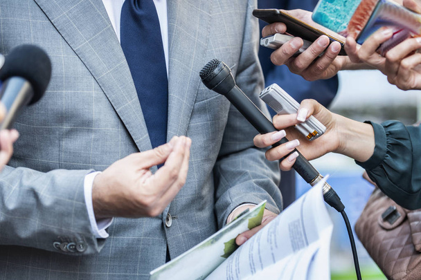 Συνέντευξη Τύπου - δημοσιογράφοι με μικρόφωνα παίρνουν συνέντευξη από επίσημα ντυμένο πολιτικό ή επιχειρηματία. - Φωτογραφία, εικόνα