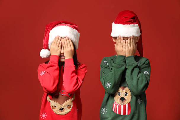 Cute dzieci w swetrach świątecznych i Santa kapelusze na tle koloru - Zdjęcie, obraz