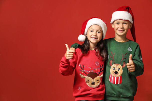Enfants mignons en pulls de Noël et chapeaux de Père Noël montrant pouce vers le haut sur fond de couleur
 - Photo, image
