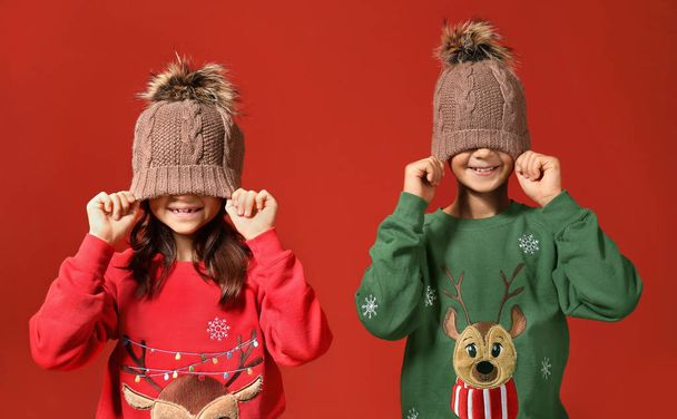 Милі діти в різдвяних светрах і капелюхах на кольоровому фоні
 - Фото, зображення