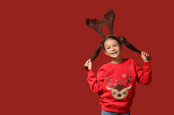 Roztomilé dívka v vánoční svetr a jelení rohy na barevném pozadí - Fotografie, Obrázek