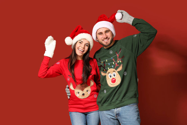 Young couple in Christmas sweaters and Santa hats on color background - Foto, imagen