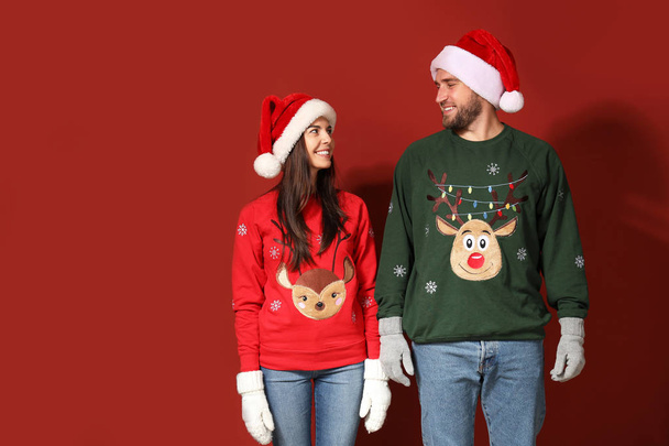 Young couple in Christmas sweaters and Santa hats on color background - Фото, зображення