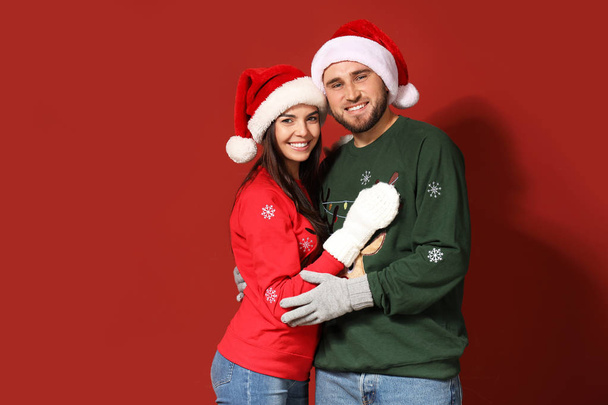 Young couple in Christmas sweaters and Santa hats on color background - Fotografie, Obrázek