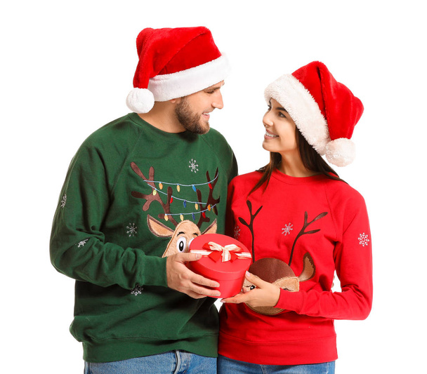 Young couple in Christmas sweaters and with gift on white background - Photo, Image