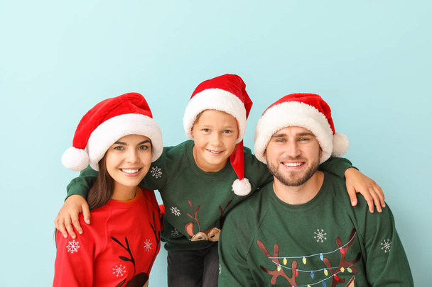 Happy family in Christmas sweaters and Santa hats on color background - Photo, Image