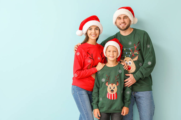 Happy family in Christmas sweaters and Santa hats on color background - 写真・画像