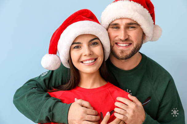 Счастливая пара в рождественских свитерах и шляпах Санты на цветном фоне
 - Фото, изображение