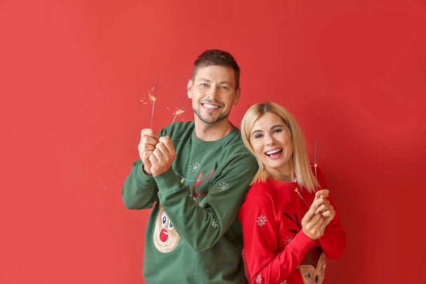 Happy couple with Christmas sparklers on color background - Photo, image
