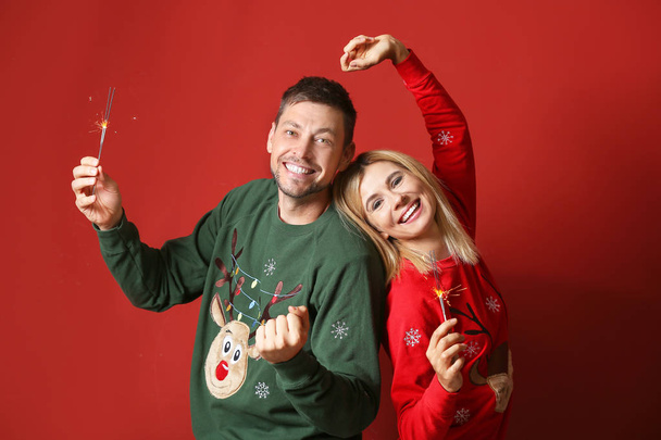 Happy couple with Christmas sparklers on color background - Photo, Image