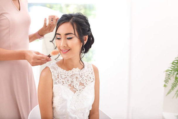 Professionele make-up artiest werken met jonge Aziatische bruid thuis - Foto, afbeelding