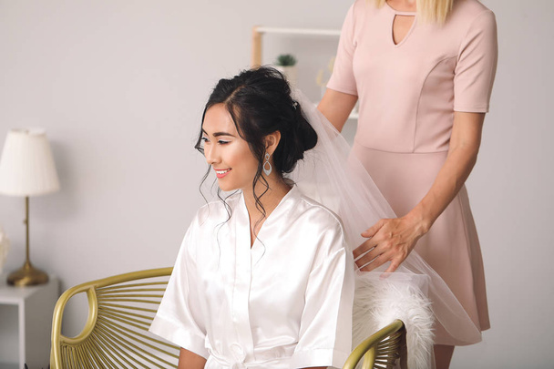 Professional hairdresser working with young Asian bride at home - Foto, Bild