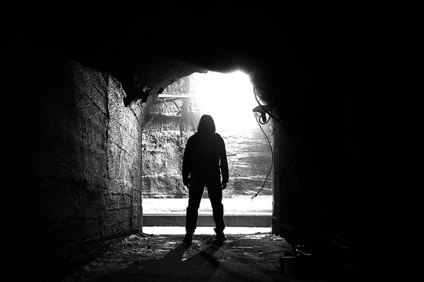 Ένας άντρας στέκεται σε ένα υπόγειο διάδρομο. Άνθρωπος στο τούνελ ασπρόμαυρος. - Φωτογραφία, εικόνα