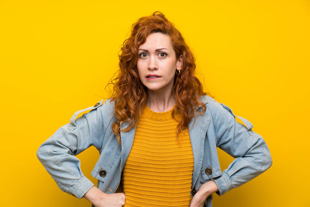 Redhead vrouw over geïsoleerde gele achtergrond hebben twijfels en met verwarring gezichtsuitdrukking - Foto, afbeelding