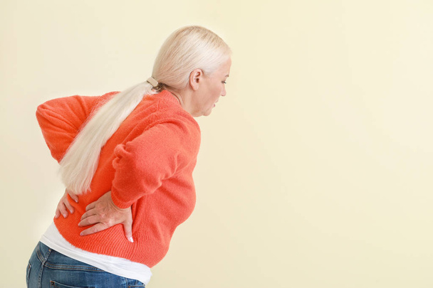 Mature woman suffering from back pain on light background - Zdjęcie, obraz