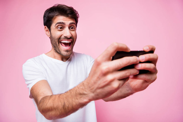 Portrait of funky funny interested cheerful middle eastern man hold use his smartphone play internet video game race wear style outfit isolated over pink color background - Photo, Image