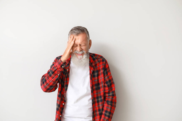 Senior man suffering from headache on light background - Foto, afbeelding