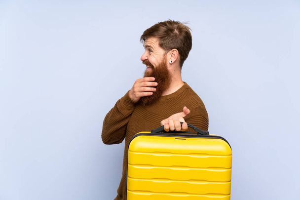Homem ruivo com barba comprida segurando uma mala pensando em uma ideia e olhando para o lado
 - Foto, Imagem