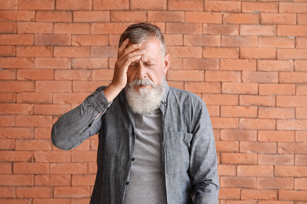 Senior man suffering from headache against brick wall - Photo, image