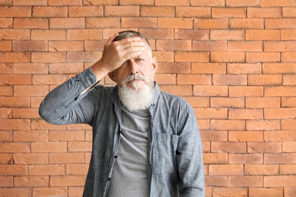 Senior man suffering from headache against brick wall - Foto, afbeelding