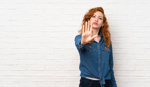 roodharige vrouw over witte bakstenen muur maken stop gebaar - Foto, afbeelding