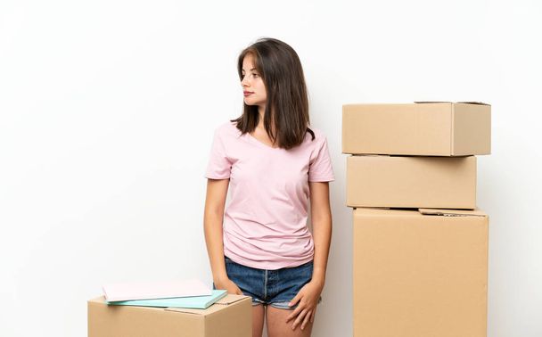 Молодая девушка переезжает в новый дом среди коробок глядя на сторону
 - Фото, изображение
