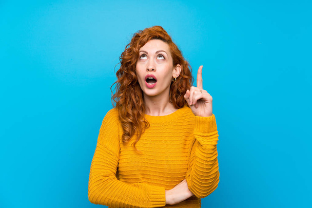 Redhead woman with yellow sweater pointing up and surprised - Photo, Image