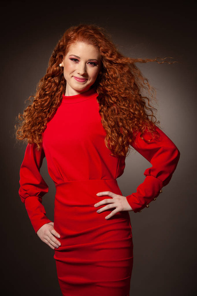 Beauty portrait of a preety redhead in red elegant dress over gr - Фото, изображение
