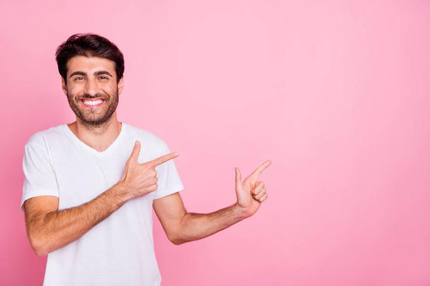 Portrait of positive cheerful middle eastern man point index finger promo show adverts recommend discounts wear white trend clothes isolated over pink color background - 写真・画像