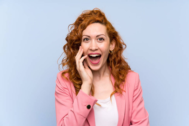Redhead woman in suit over isolated blue wall with surprise and shocked facial expression - Fotoğraf, Görsel