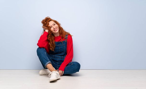 Redhead woman with overalls sitting on the floor thinking an idea - Фото, изображение