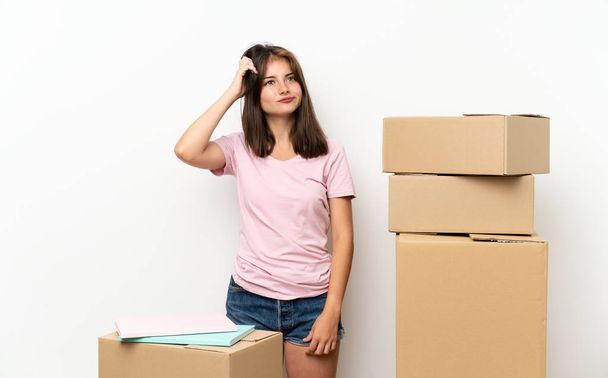Молодая девушка переезжает в новый дом среди коробок с сомнениями и с запутанным выражением лица
 - Фото, изображение