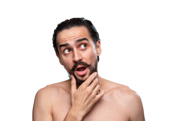 Pensativo hombre barbudo guapo con bigotes de pie desnudo aislado sobre fondo blanco y mirando a la cámara. Concepto de tratamiento matutino. Rutina matinal
 - Foto, Imagen