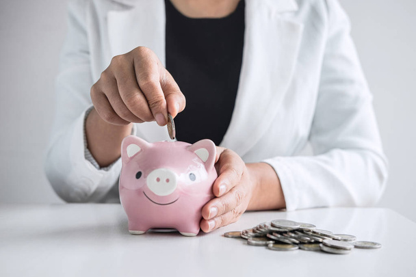 Business woman putting coin into pink piggy bank for planning st - Fotó, kép