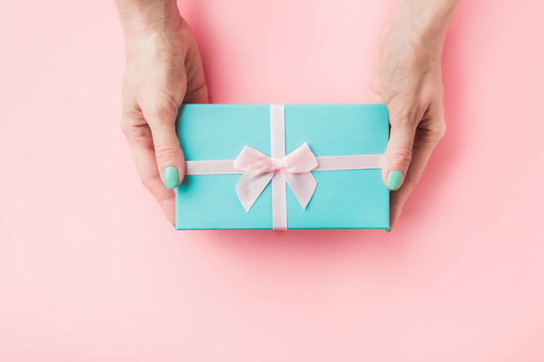 Blue gift box in female hand on pastel pink. - Valokuva, kuva