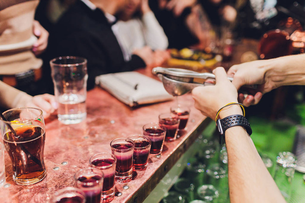 Bartender pouring strong alcoholic drink into small glasses on bar, shots. - Foto, Bild